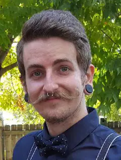 Mann mit Bart und Fliege steht im Garten und lächelt in die Kamera.