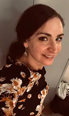 Frau mit dunklem Haar und Blumenmuster-Kleid lächelt in die Kamera.