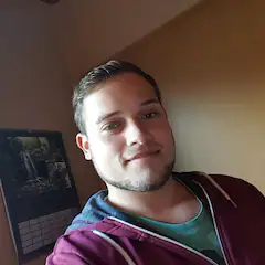 Mann mit kurzem Haar lächelt in einem Zimmer in die Kamera.