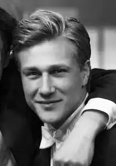 Porträt eines jungen Mannes im Anzug, der freundlich in die Kamera lächelt.