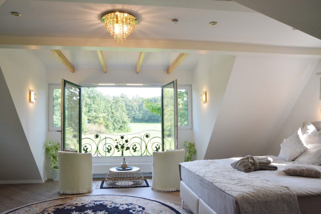 Helles Schlafzimmer mit Balkonblick ins Grüne und elegantem Kronleuchter.