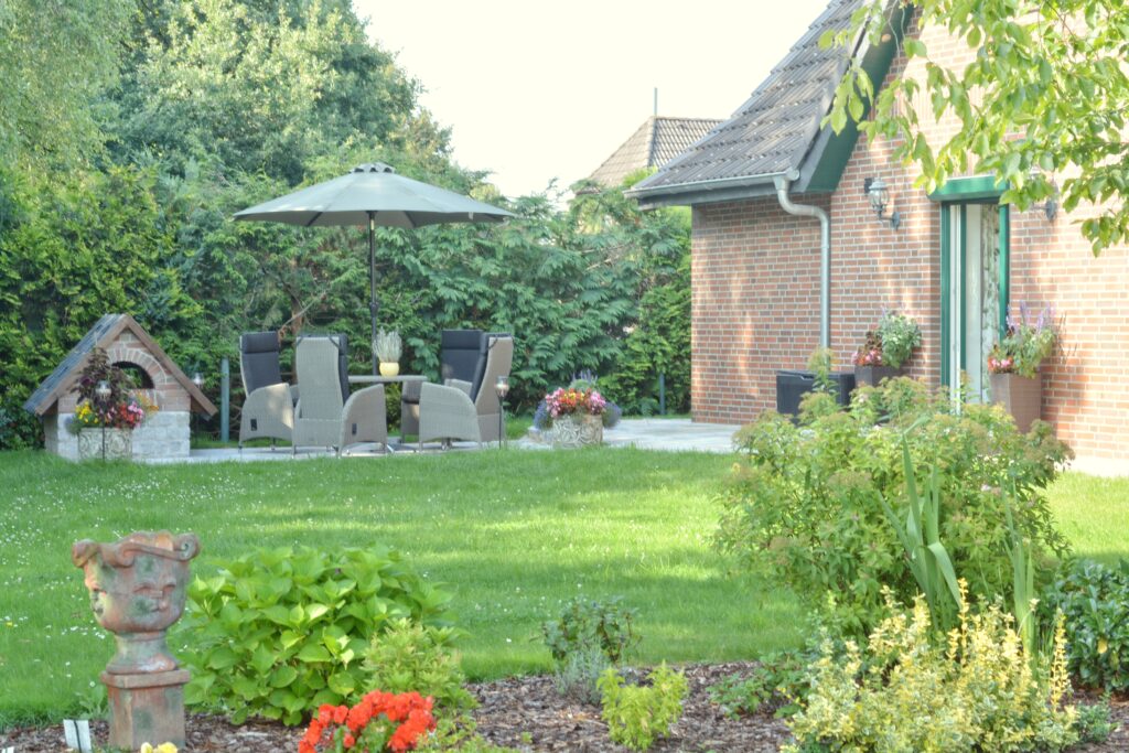 Gepflegter Garten mit Terrasse, Sitzgruppe und Sonnenschirm.
