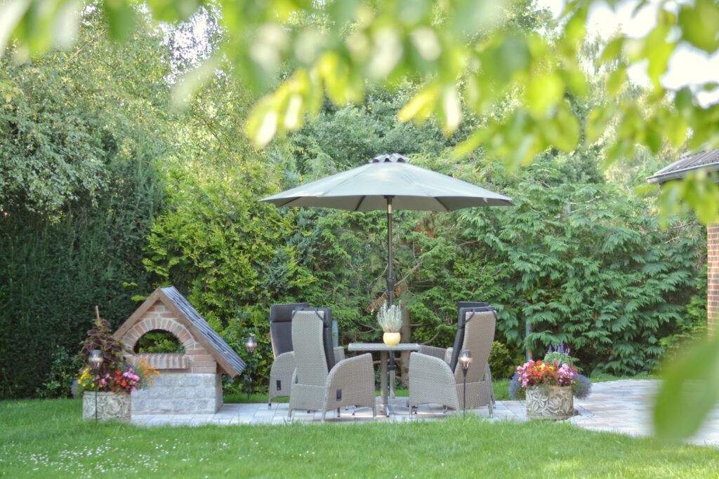 Terrasse mit Gartentisch, Stühlen und Sonnenschirm im Grünen.