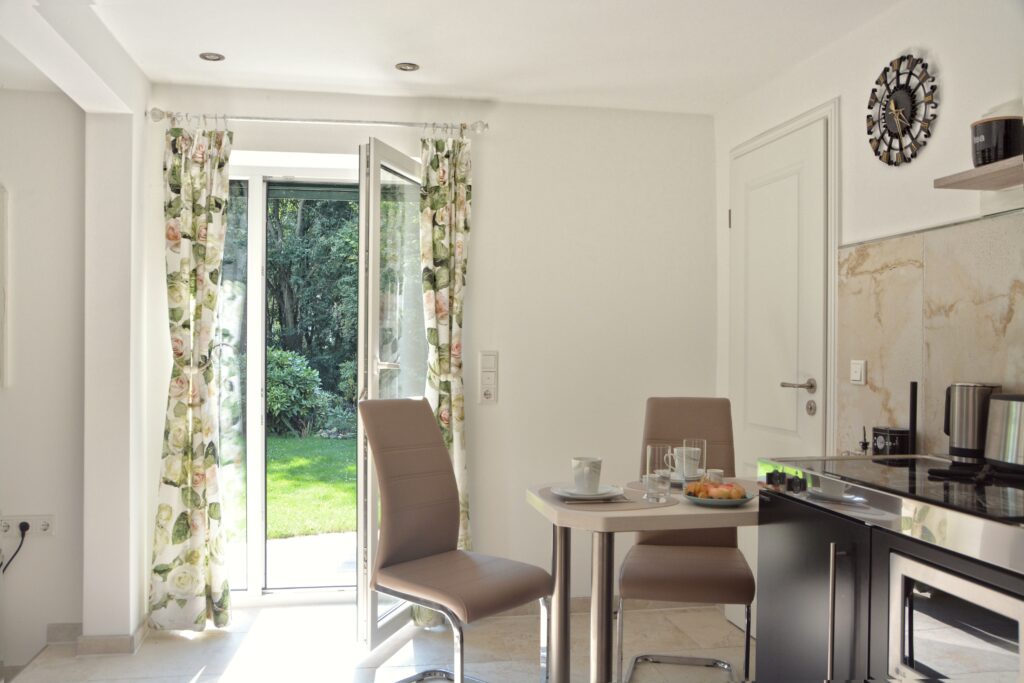 Helle Küchenzeile mit Esstisch und offener Tür zum Garten.